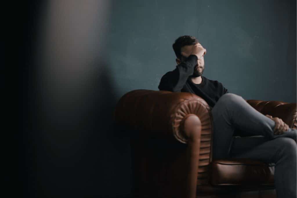 A man sitting on a sofa with his head in his hands struggling to detox from drugs alone