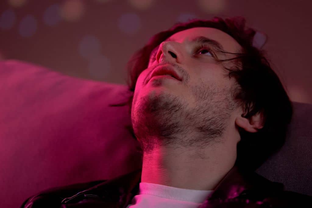 A man with a cocaine addiction with cocaine at nose feeling high at rave party, lying back on a sofa - Which Rehab