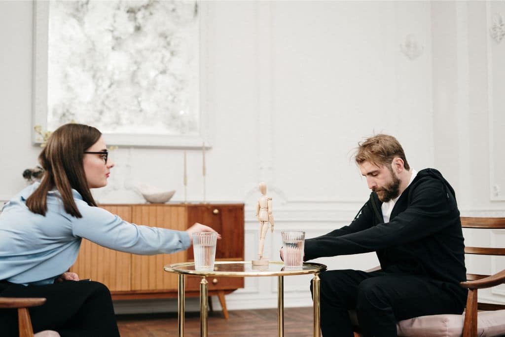 Sad man in black hoodie with a therapist in mental health consultation - Which Rehab