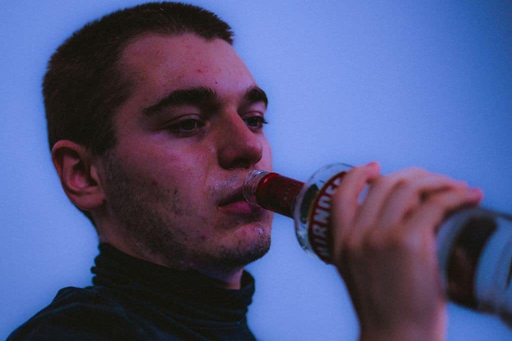 A man drinking from a vodka bottle looking sad - Which Rehab