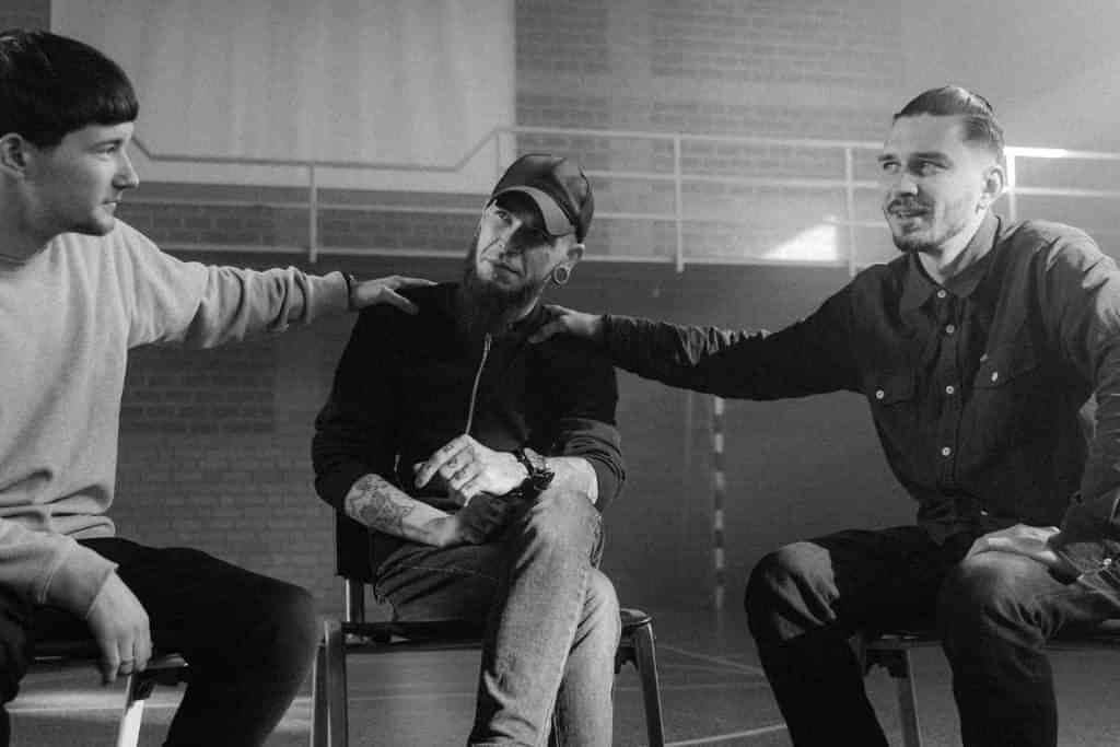 A group of men holding each others shoulders in a rehab group therapy session - Which Rehab